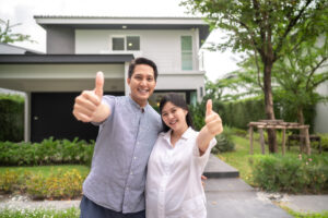 Happy customers, a couple with thumbs up standing together in front of their house